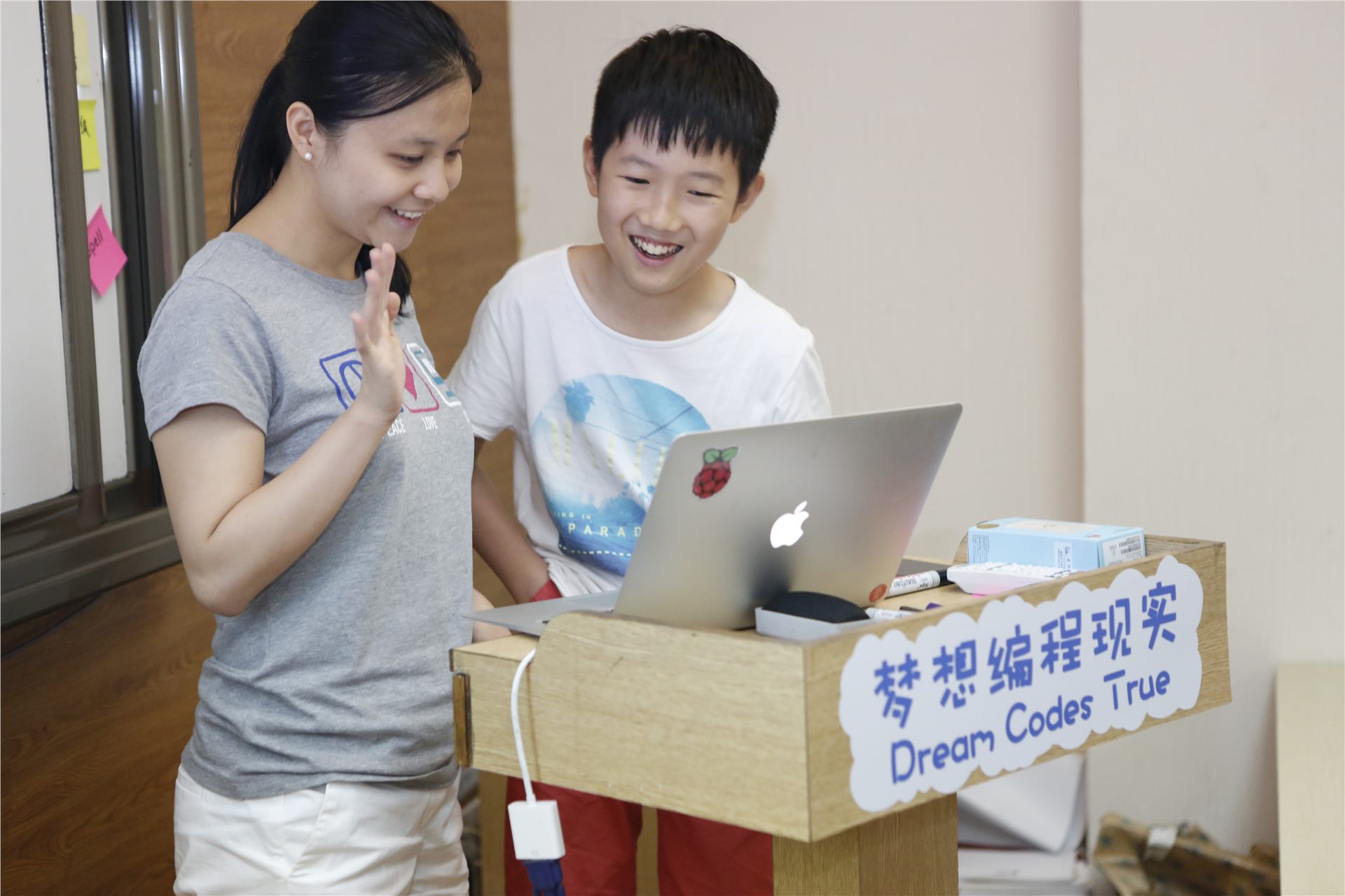 学生在展示台旁和老师一起查看电脑上的项目作品
